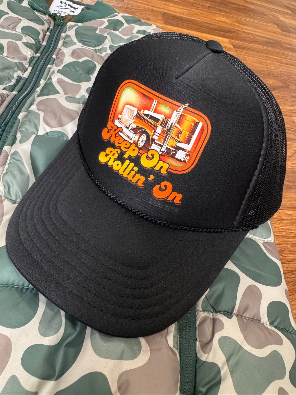 Black cap with orange and yellow design on a camouflage-patterned surface