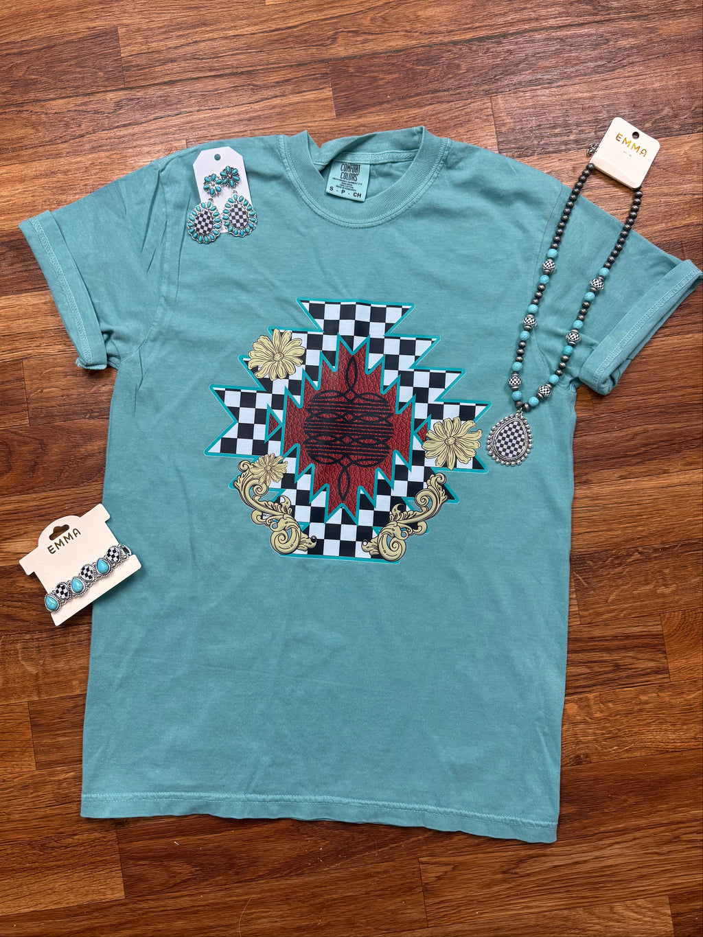 Teal t-shirt with a decorative design on a wooden floor
